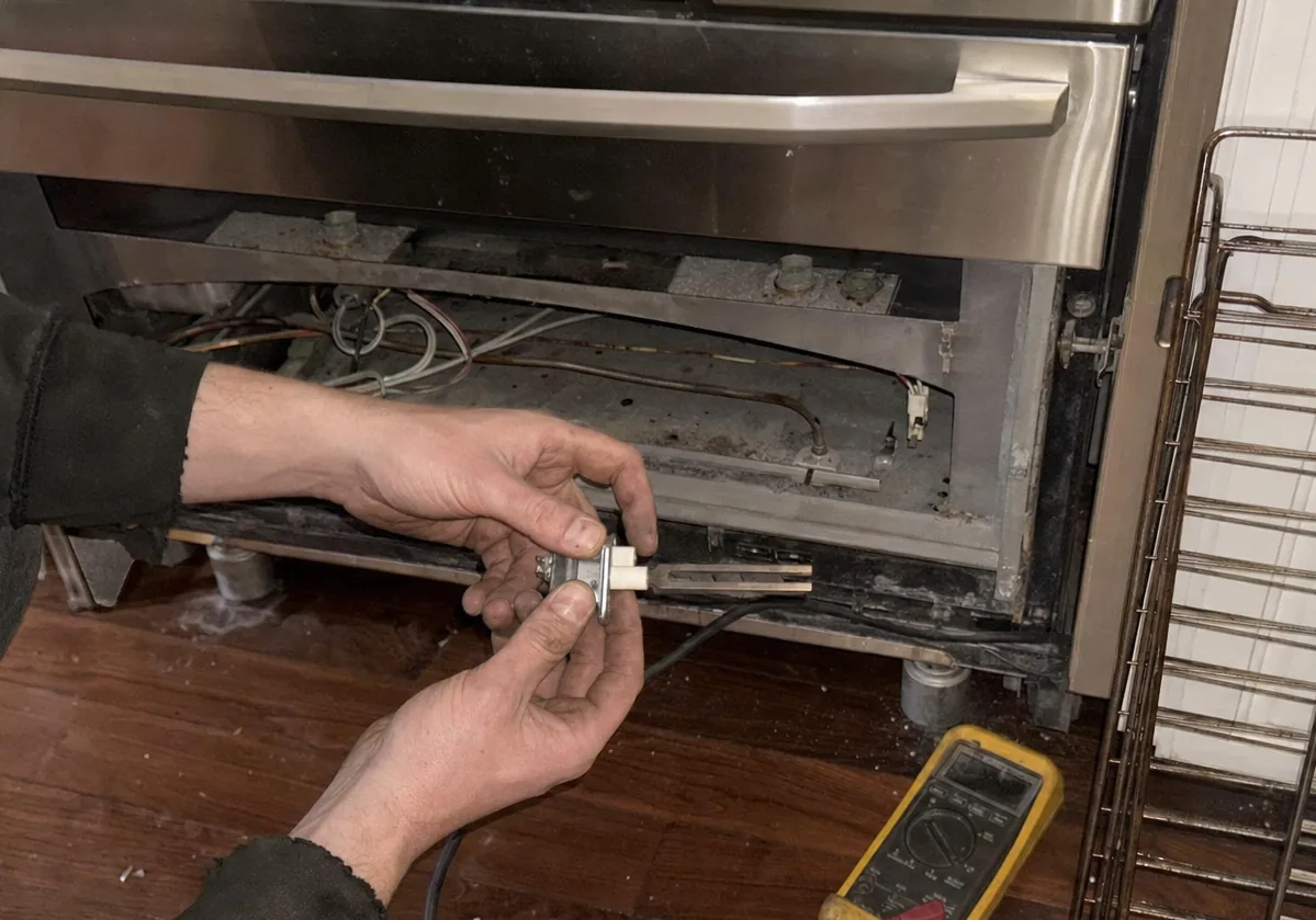 Range pulled forward in a narrow older kitchen with its lower panel off and oven racks propped against the wall behind
