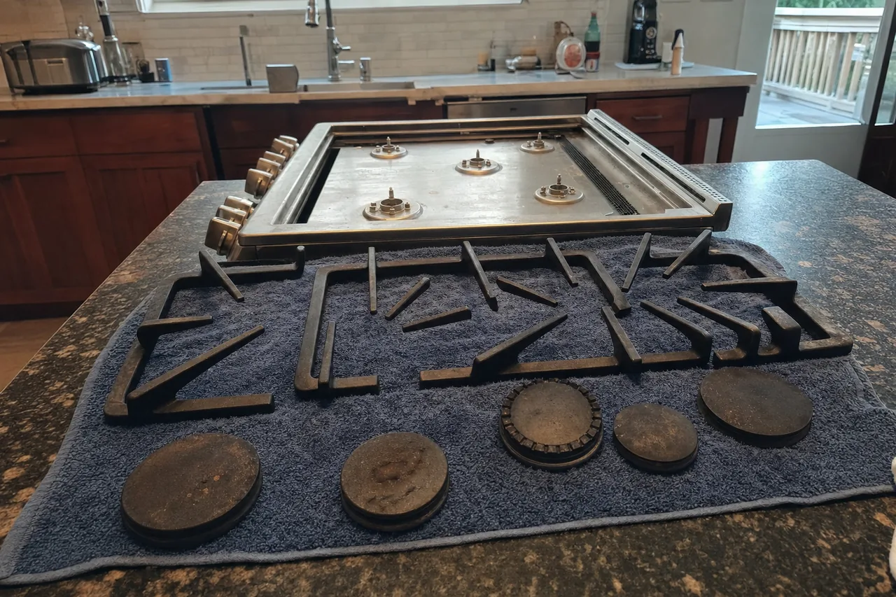 Dulled cast iron grates and pitted burner caps resting on a towel next to the stainless cooktop they were lifted out of